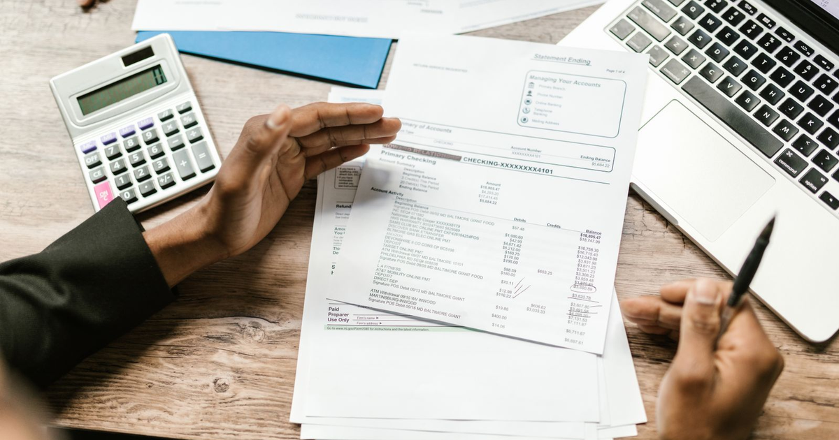 manos revisando facturas de proveedores en papel junto a una calculadora y un portátil en una mesa de oficina